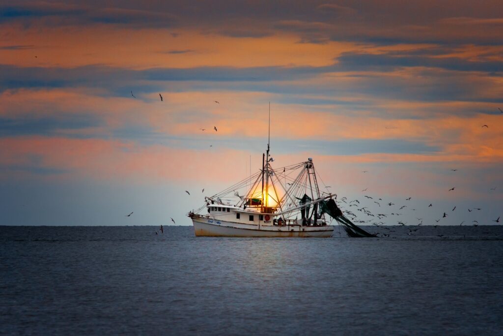 Fishing trawler in Oak Island, NC waters at sunset with seagulls overhead